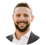 A man with short hair and a beard, wearing a suit jacket and white shirt, smiling at the camera against a light background—raising questions about online identity in the age of deepfake technology.